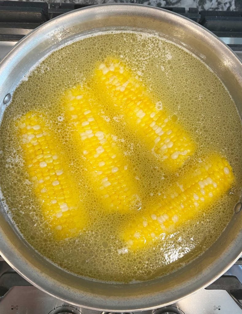 ears of corn in pot of water on stove.