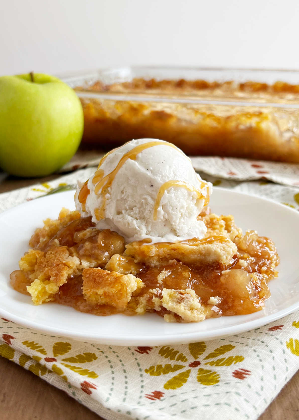 Slice of caramel apple dump cake with vanilla ice cream and caramel sauce on a plate.