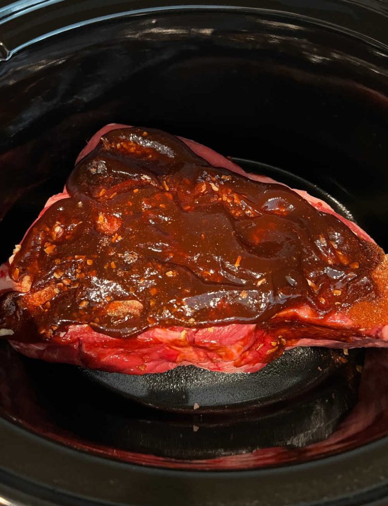 beef roast in slow cooker with bbq sauce on top.