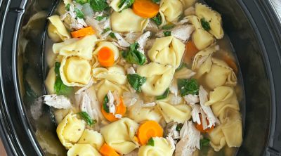 crock pot chicken tortellini soup with carrots and fresh spinach in the slow cooker.