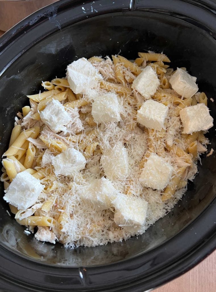 cream cheese and Parmesan cheese with chicken and pasta in crockpot.