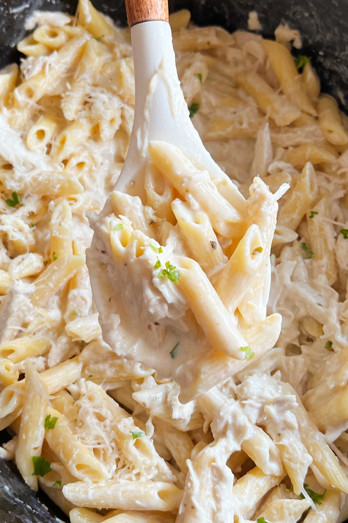 serving spoon with crock pot olive garden chicken pasta in creamy sauce in slow cooker.