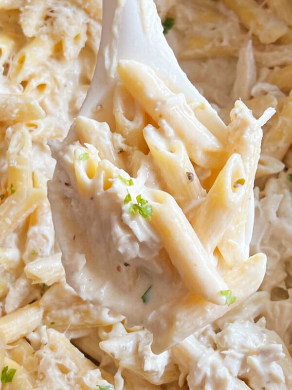 crock pot olive garden chicken pasta in creamy sauce on serving spoon in slow cooker.