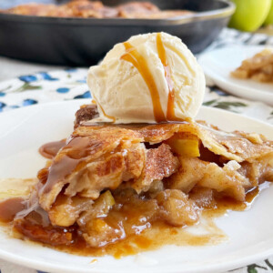 slice of skillet apple pie with ice cream and caramel sauce on plate.
