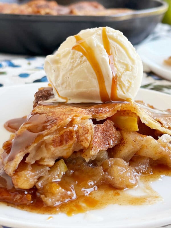 slice of skillet apple pie with ice cream and caramel sauce on plate.