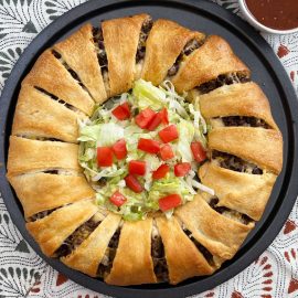 baked taco ring made with crescent rolls with shredded lettuce and tomatoes inside.