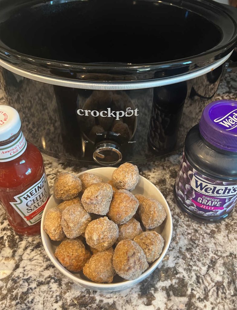 slow cooker with bottle of Heinz chili sauce, frozen meatballs and jar of grape jelly.