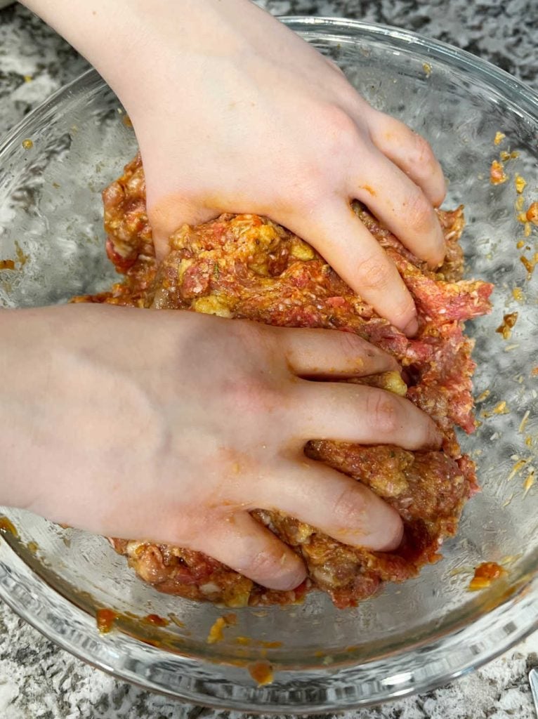 hands mixing meatloaf mixture in bowl.