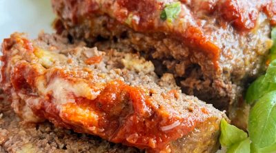 Italian meatloaf with marinara sauce and basil sliced on platter.