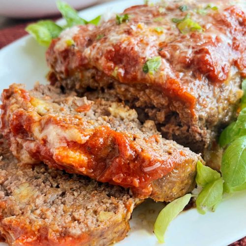 Italian meatloaf with marinara sauce and basil sliced on platter.