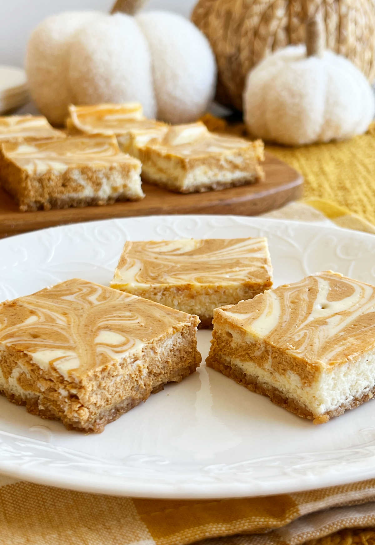 sliced pumpkin cheesecake bars on plate with pumpkins on the table.