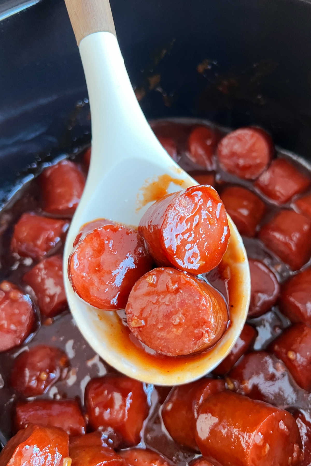 slow cooker kielbasa bites with bbq sauce in serving spoon over crock pot.