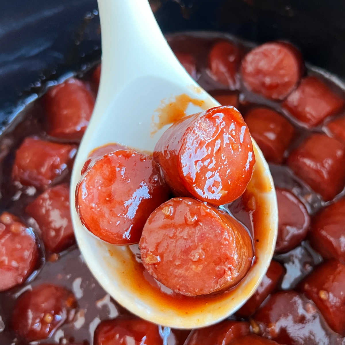 slow cooker kielbasa bites with BBQ sauce in serving spoon over crockpot.