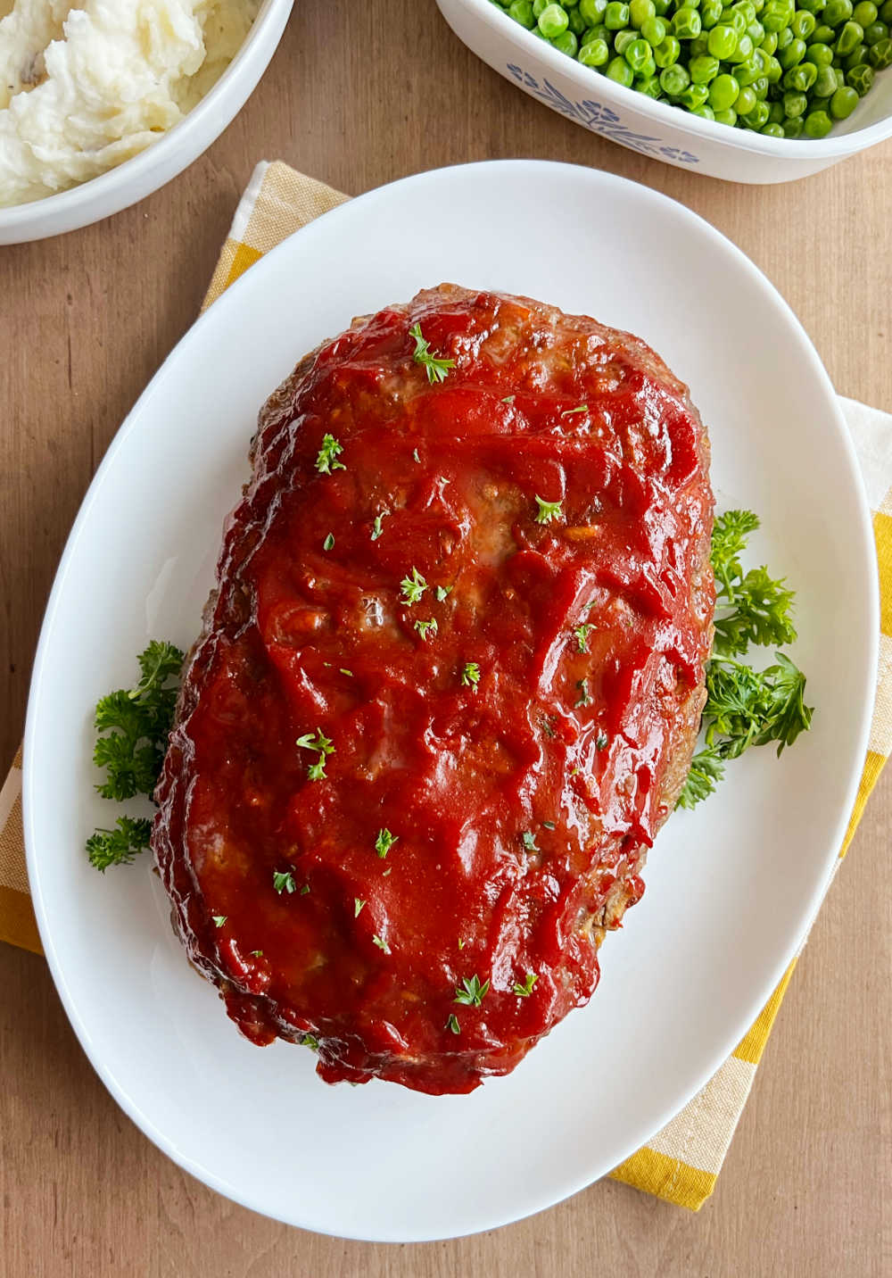 meatloaf with stuffing on a platter with parsley, mashed potatoes and peas.