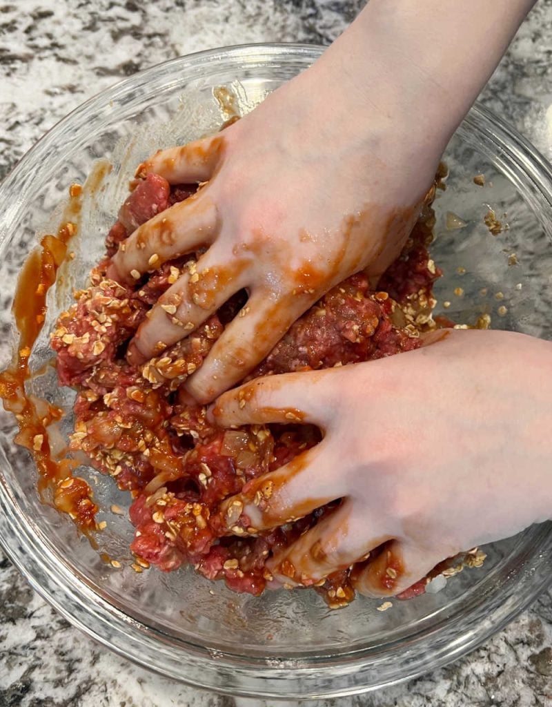 hands in ground beef mixture in bowl.