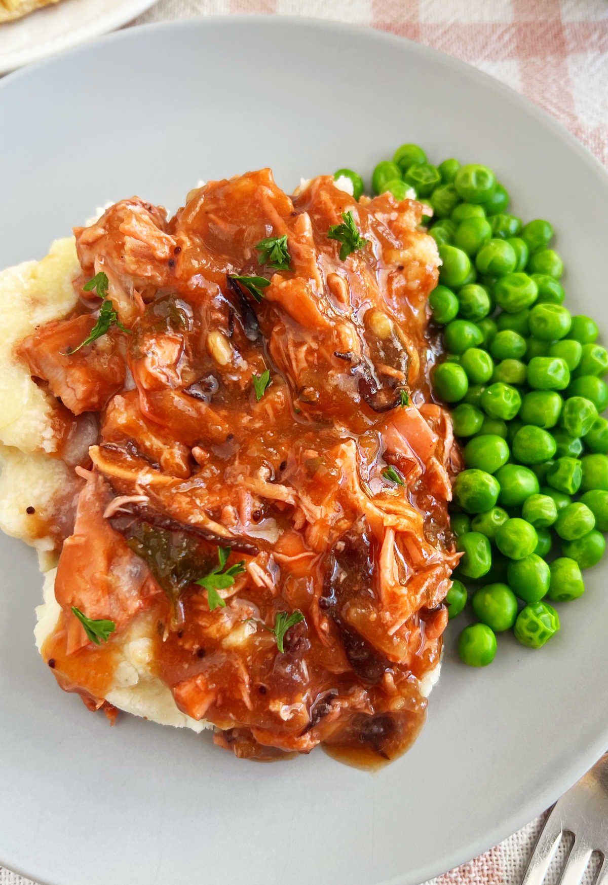 shredded cranberry chicken with mashed potatoes and peas on plate.