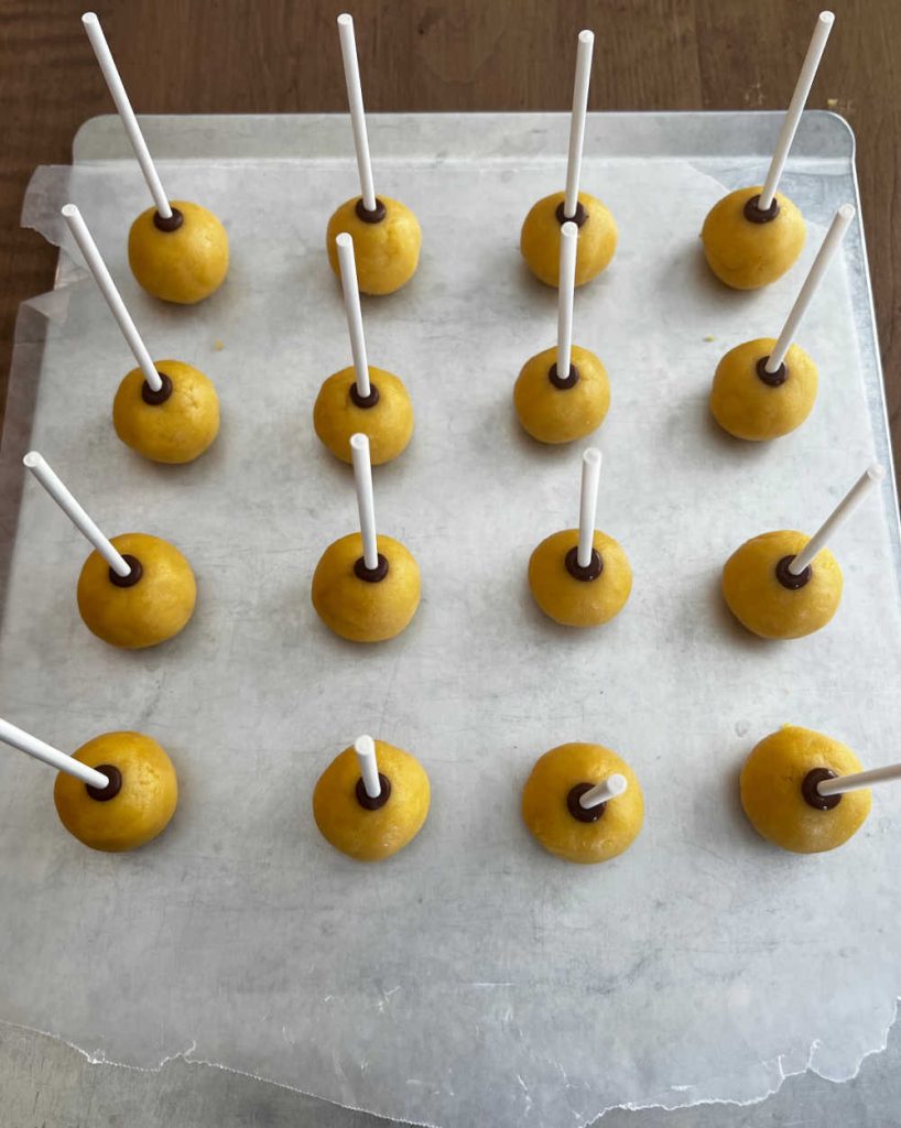 vanilla cake balls with sticks on baking sheet.
