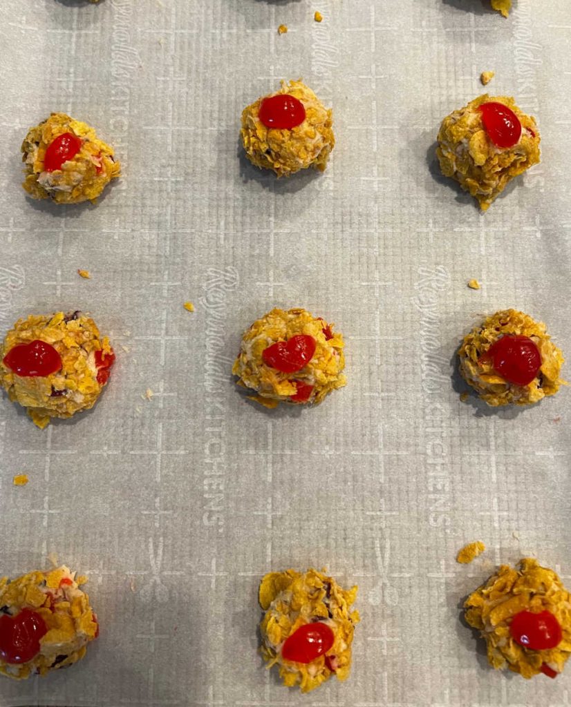 unbaked cherry winks rolled in cornflakes on parchment paper.