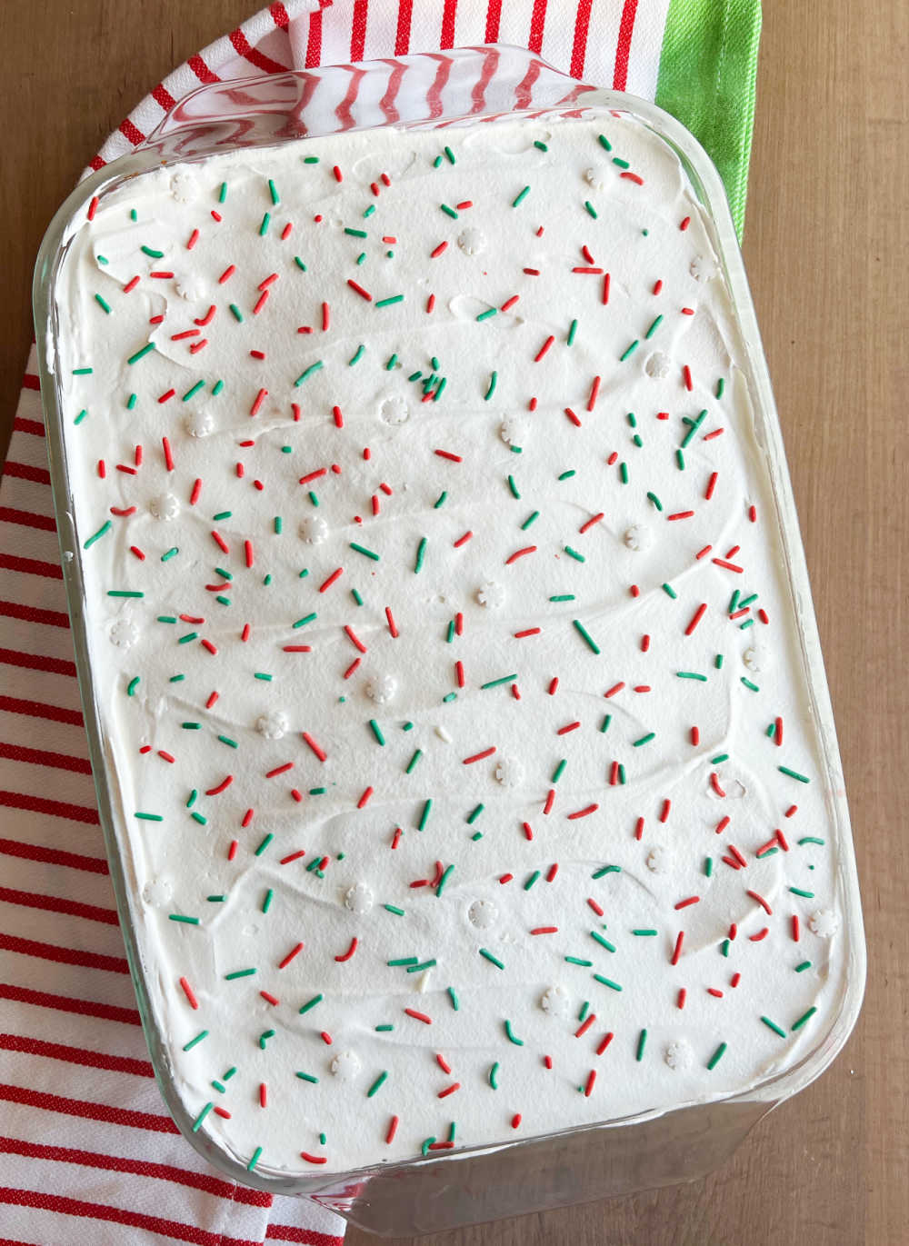christmas poke cake with cool whip and red and green sprinkles in baking dish.