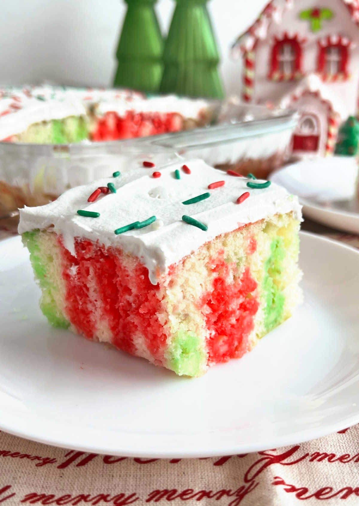 Christmas jello poke cake with cool whip frosting and holiday sprinkles on plate.