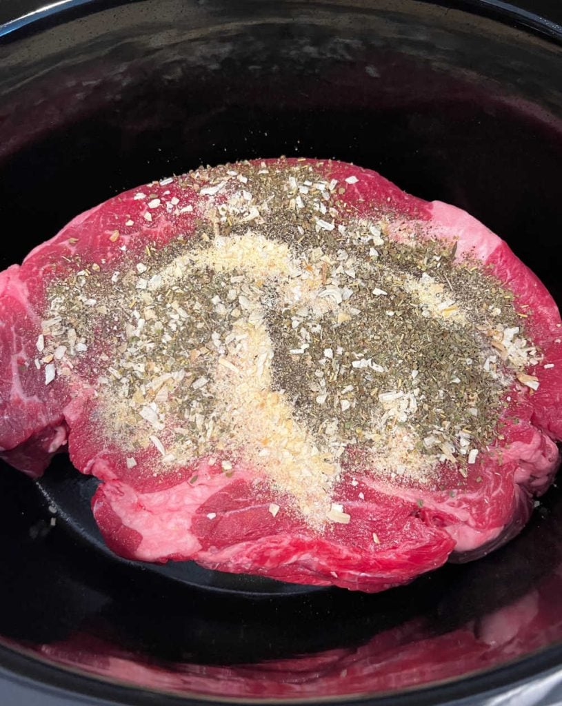 chuck roast with seasonings in a slow cooker.