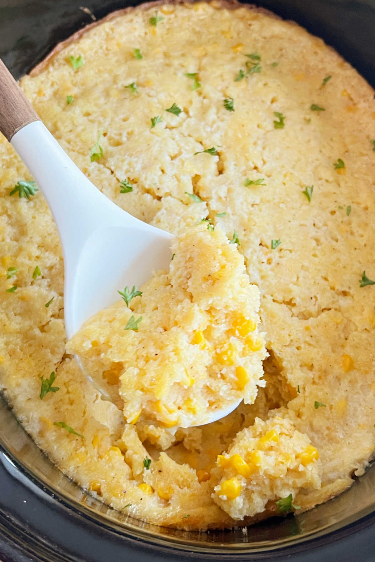 crockpot corn casserole with Jiffy Mix on a serving spoon.