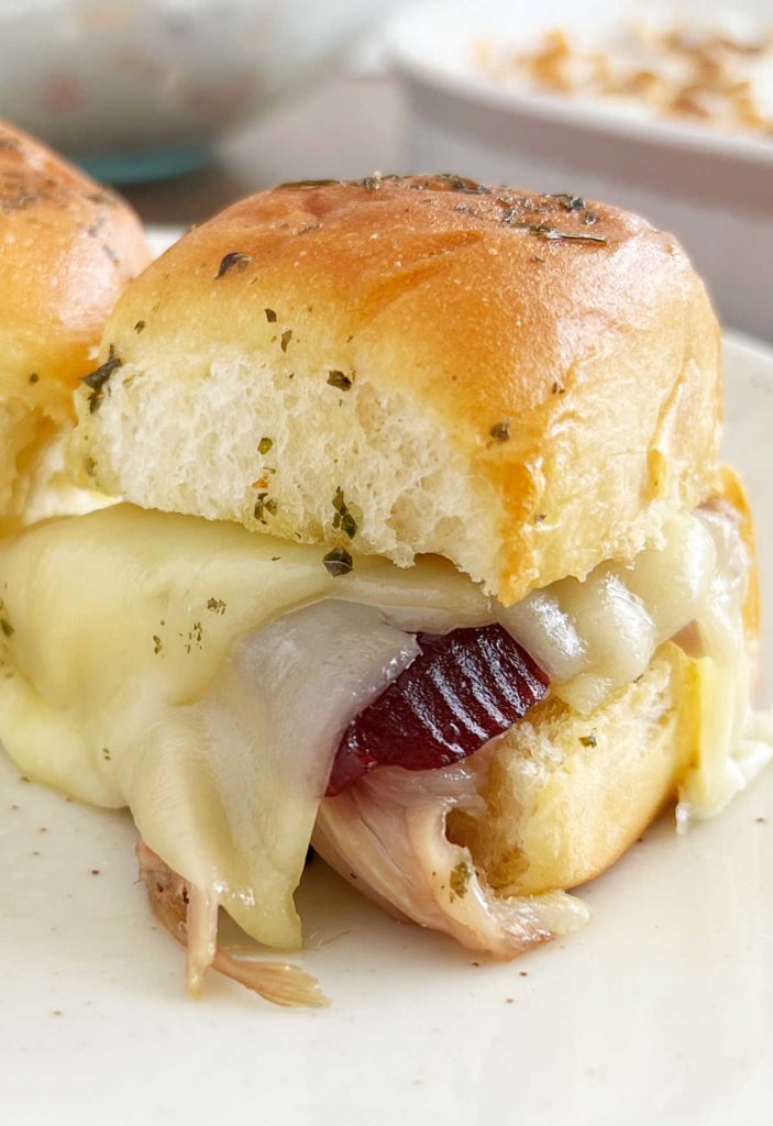 close up of baked turkey sliders with cranberry and cheese on plate.