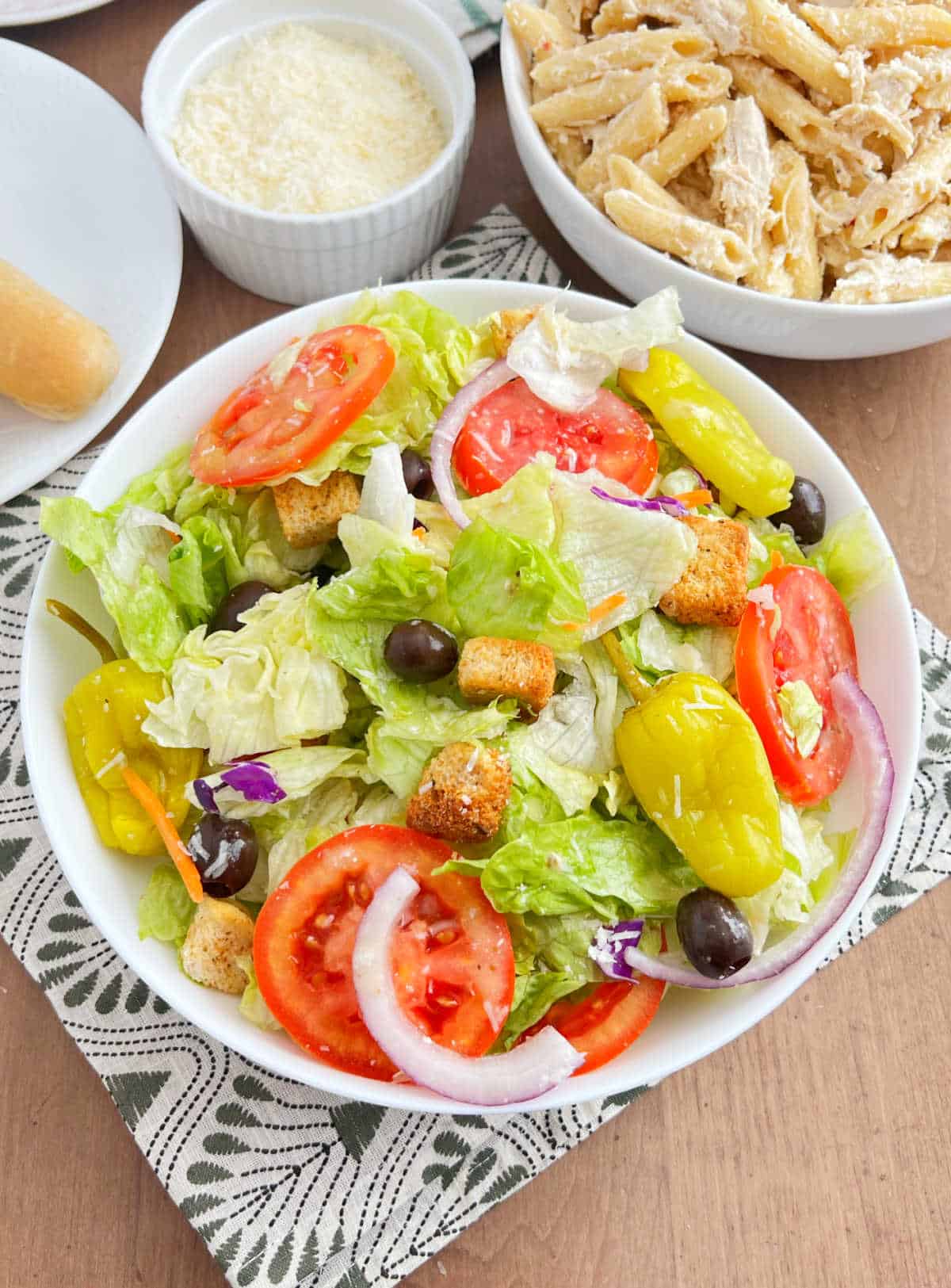copycat olive garden salad in a bowl on the table with pasta and breadsticks.