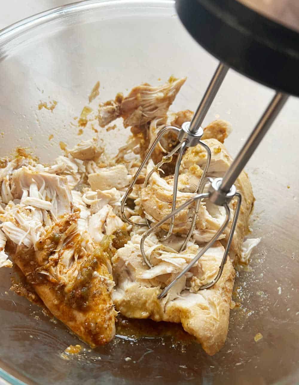 shred chicken with hand mixer in mixing bowl.