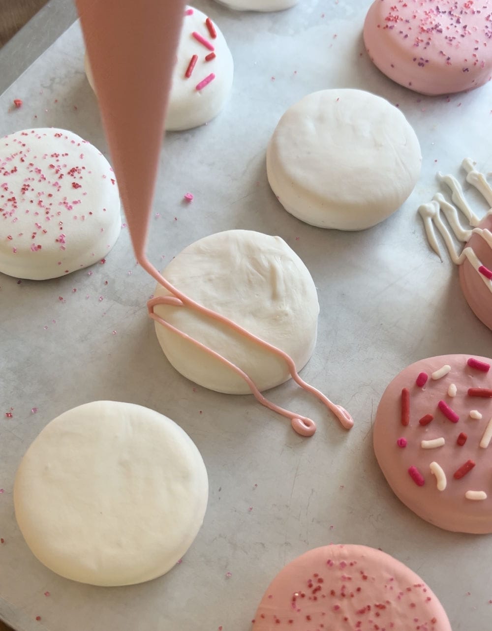 drizzle pink candy coating on white chocolate oreo cookies.
