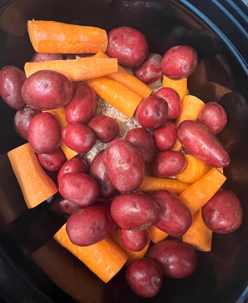 flat cut corn beef in slow cooker with carrots and potatoes on top.