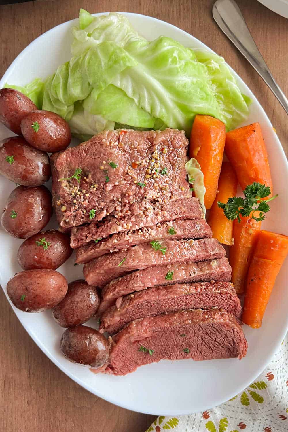 sliced corned beef brisket with baby red potatoes, green cabbage and carrots on platter.