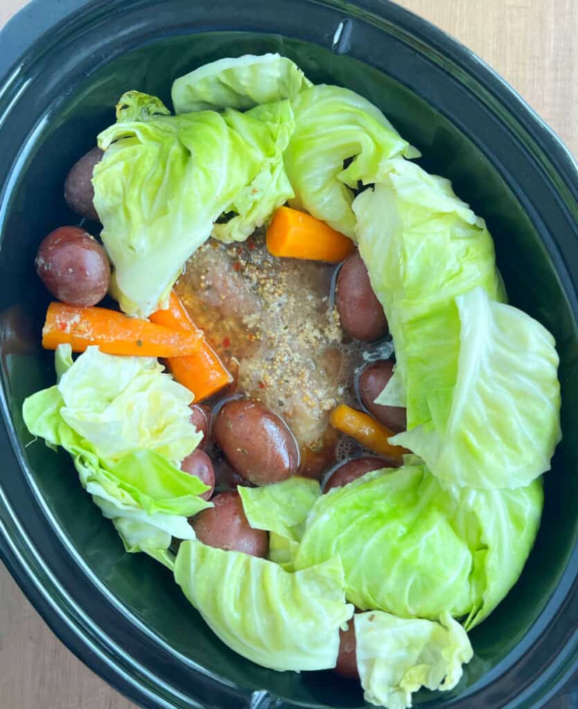 green cabbage in slow cooker with carrots, red potatoes and beef.