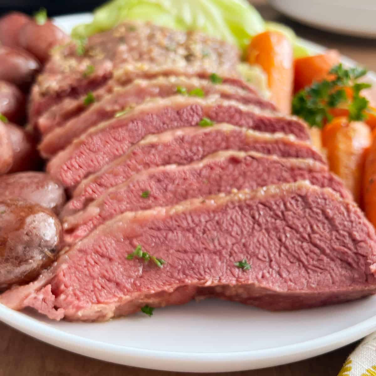 sliced crock pot corned beef with cabbage, carrots and potatoes on platter,