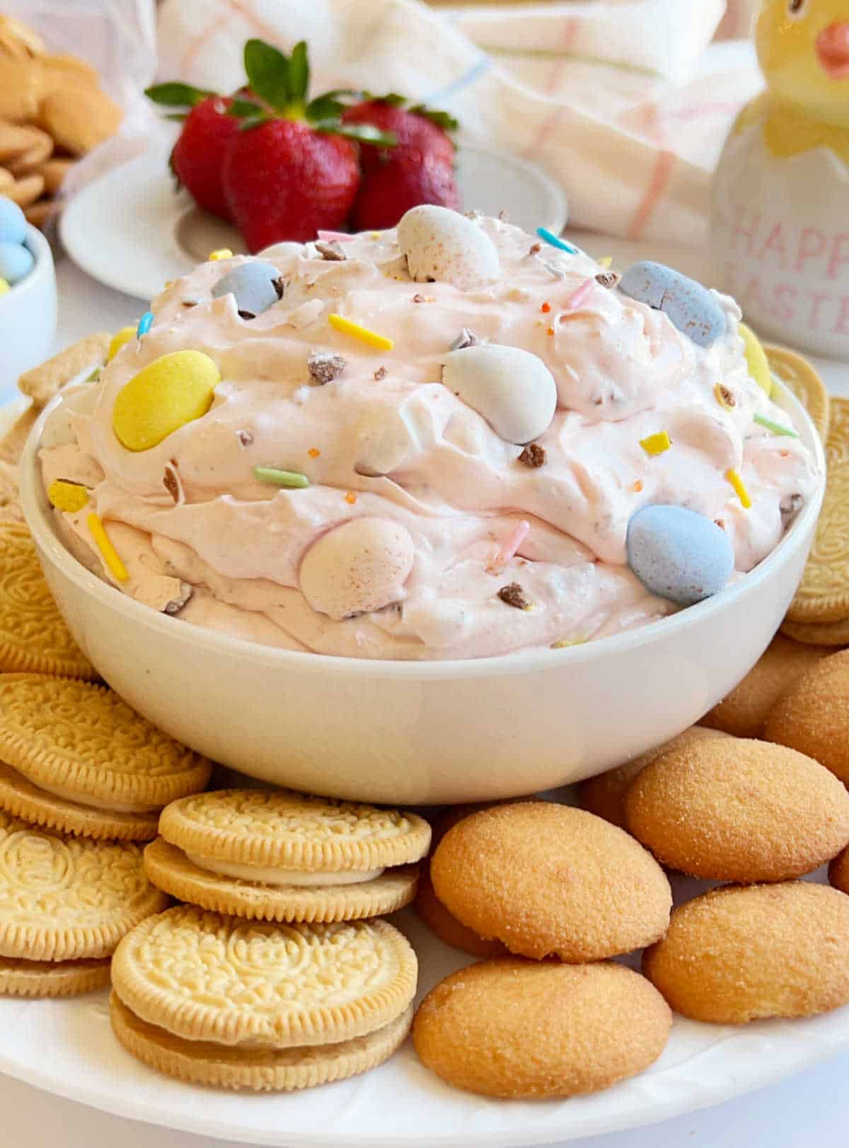 cadbury mini egg cheesecake dip in bowl with cookies and strawberries.