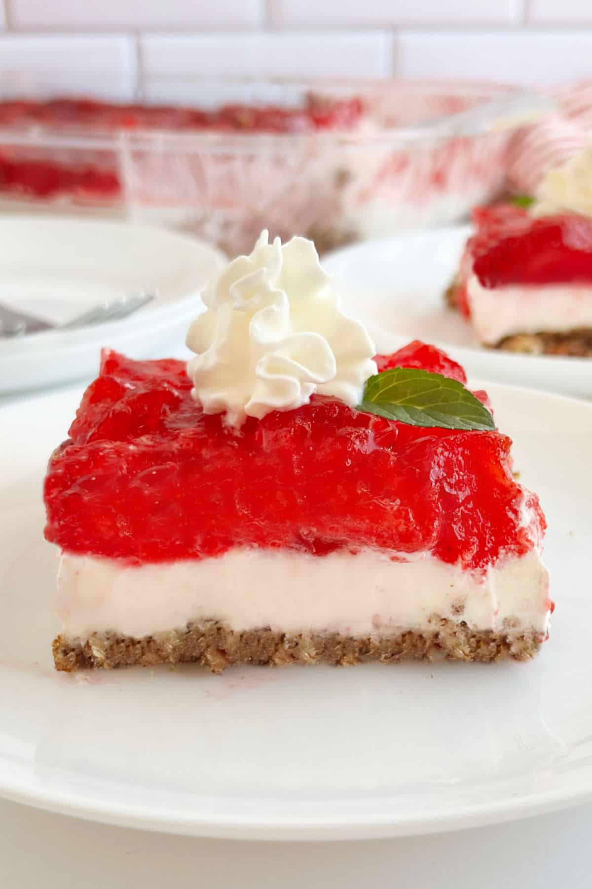 slice of strawberry pretzel salad with whipped cream and mint leaf on a plate.