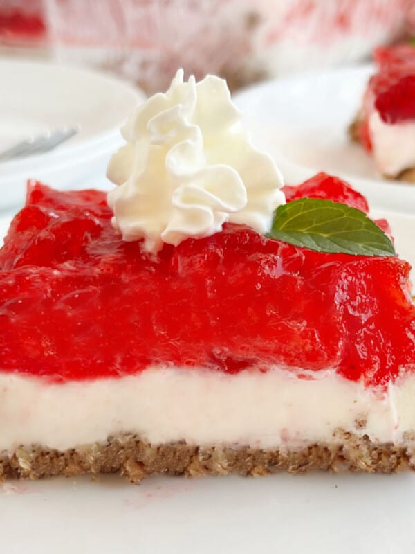 slice of strawberry pretzel salad with whipped cream on a plate.