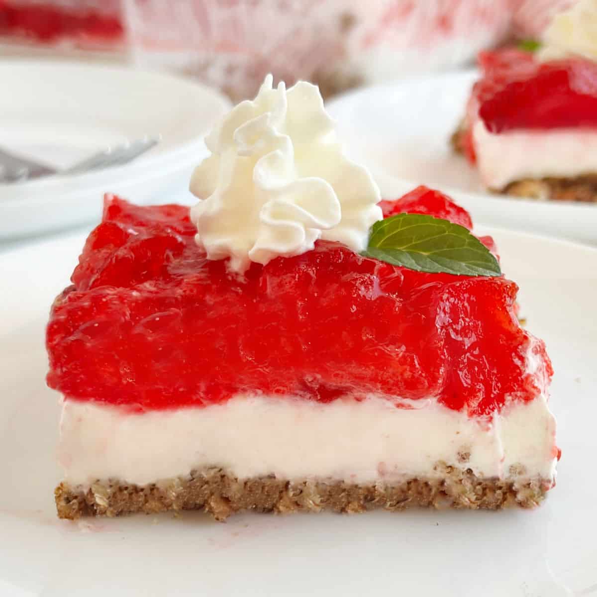 slice of strawberry pretzel salad with whipped cream on a plate.