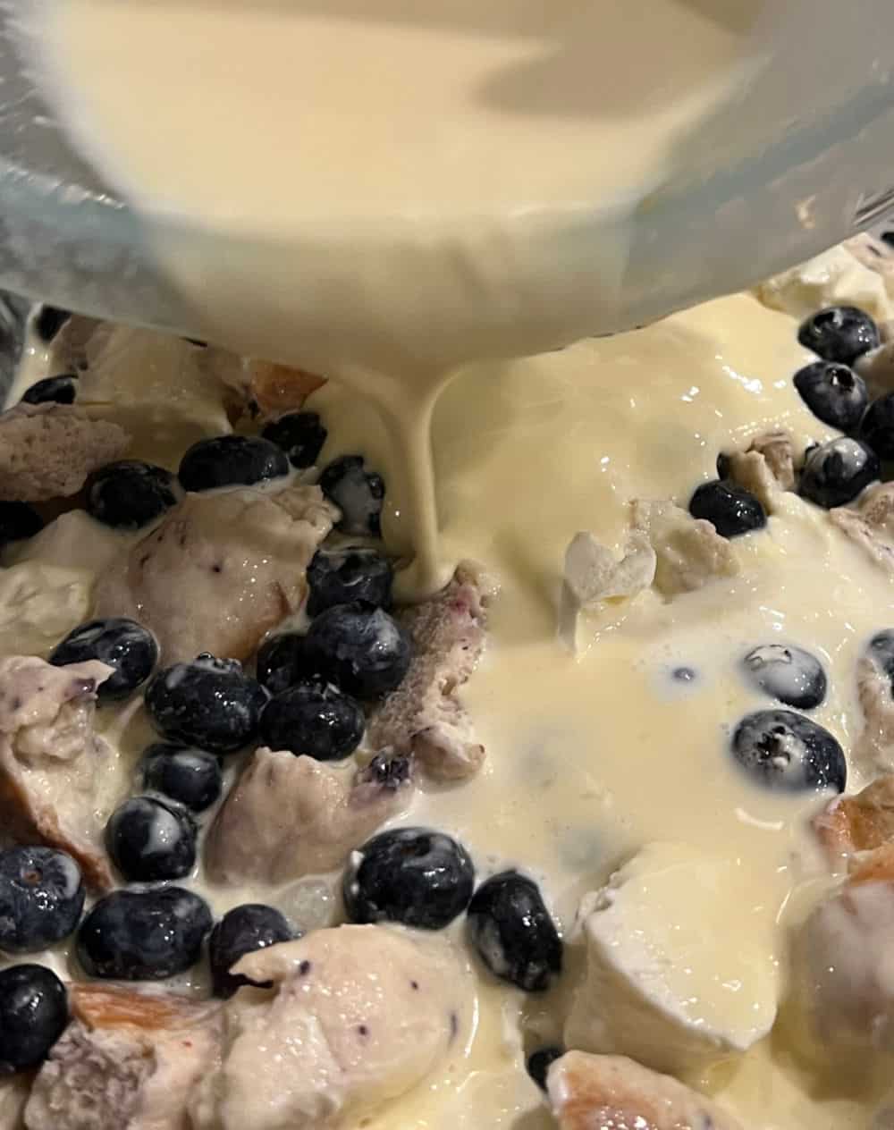 pour custard over bagels and blueberries.