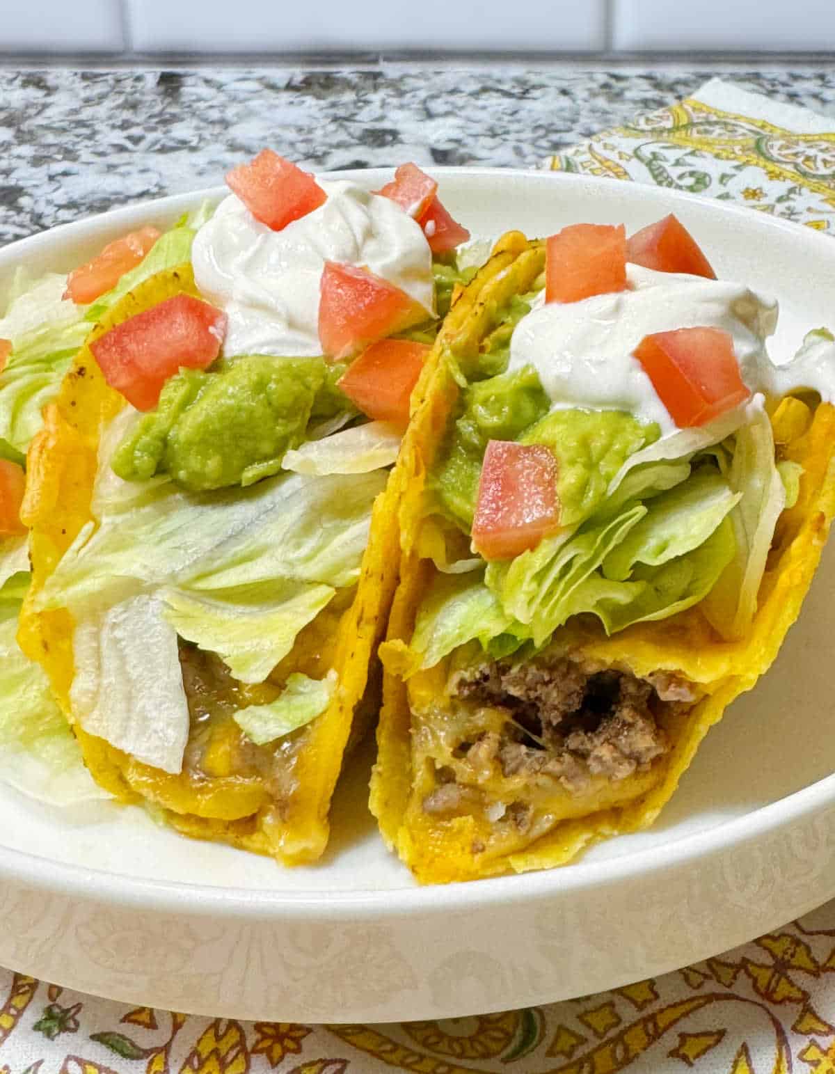 two baked tacos with ground beef and taco toppings on a dish.