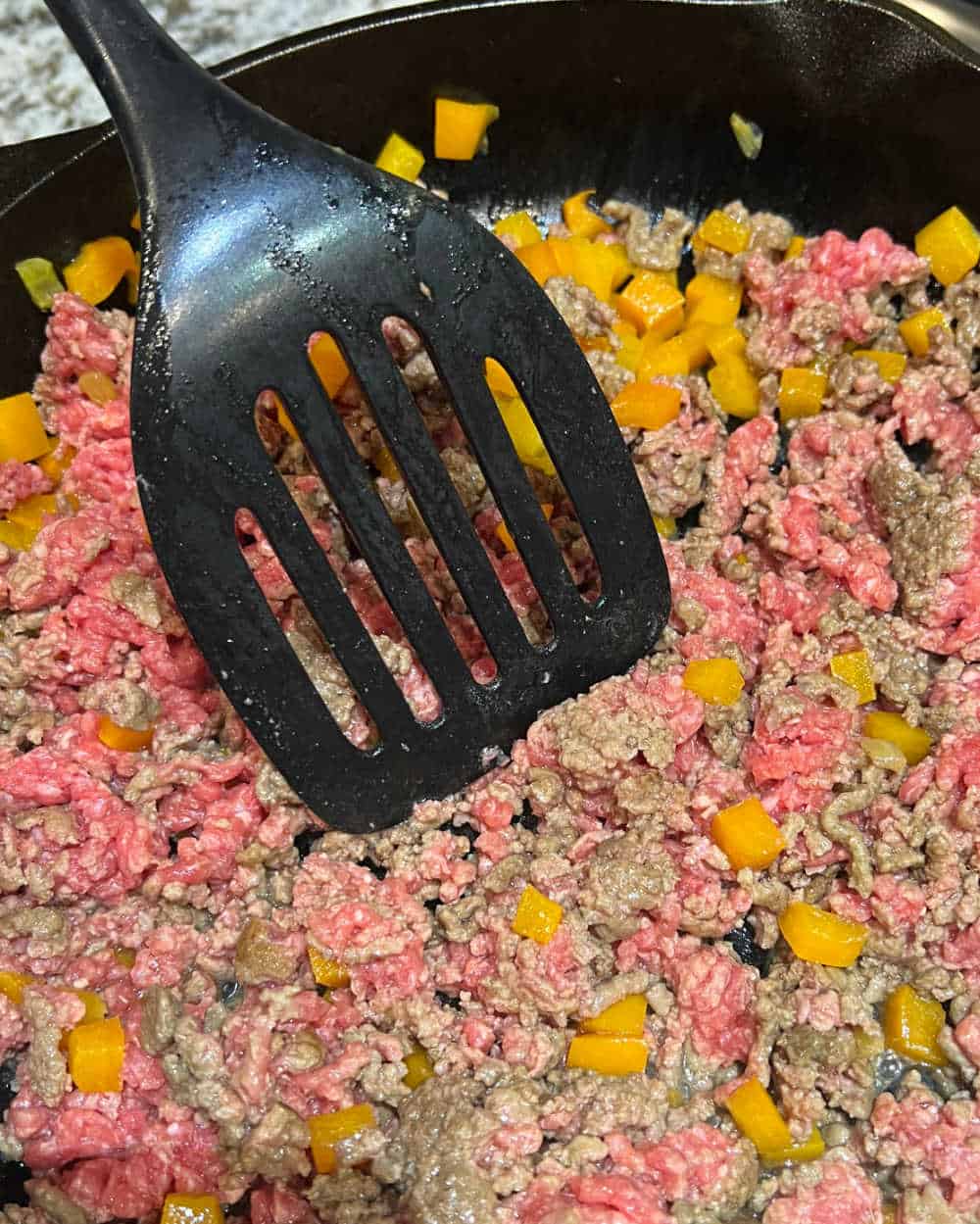 ground beef in skillet with yellow bell peppers.