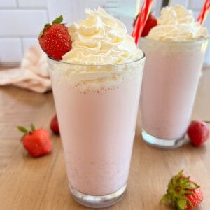 homemade strawberry milkshake with whipped cream and fresh strawberry in glass.