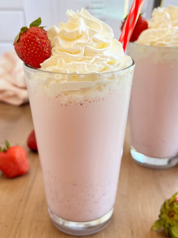 homemade strawberry milkshake with whipped cream and fresh strawberry in glass.