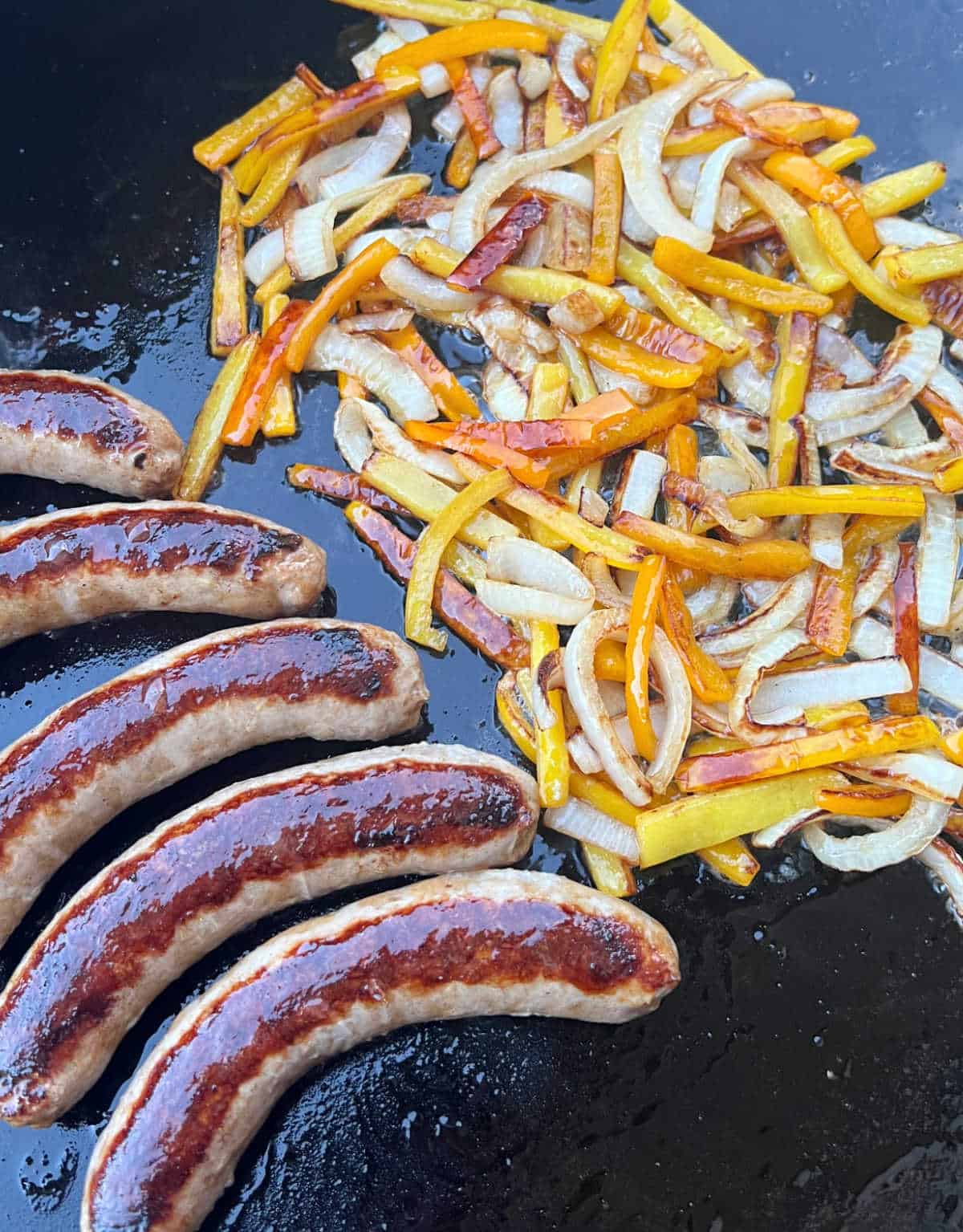 italian sausages with bell peppers and onions on blackstone griddle.