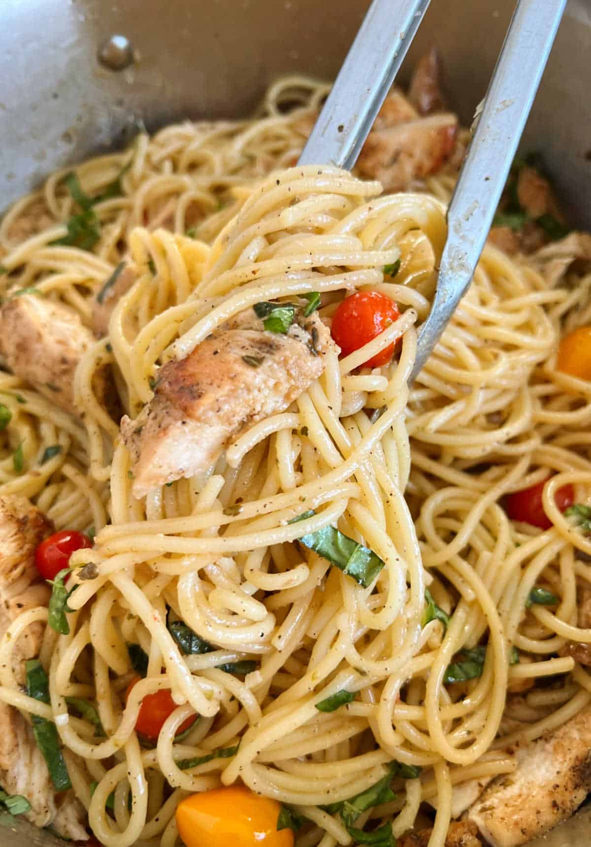 pasta with fresh tomatoes and basil and chicken in tongs.