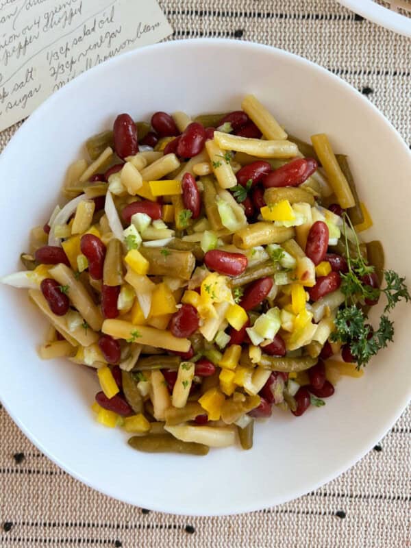 three bean salad in a white serving bowl with original recipe card.