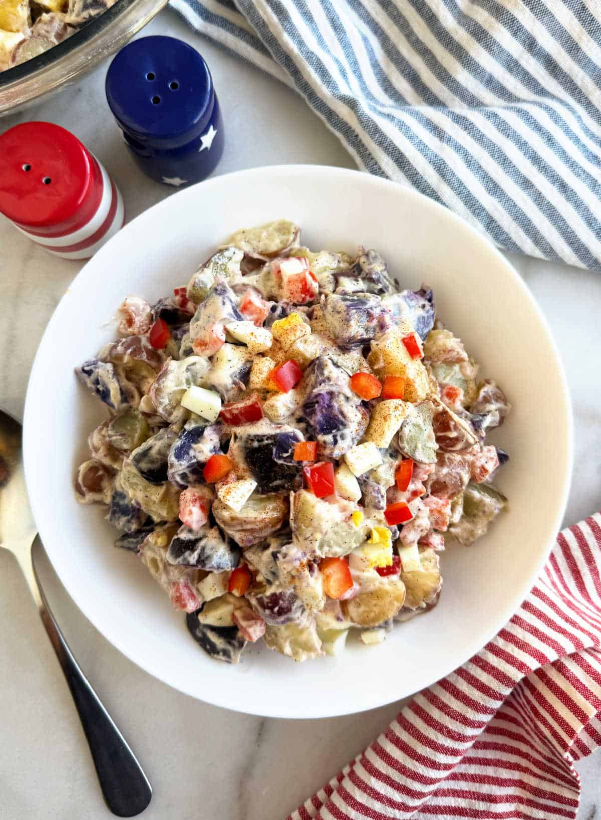red white and blue potato salad in white bowl with patriotic decor.