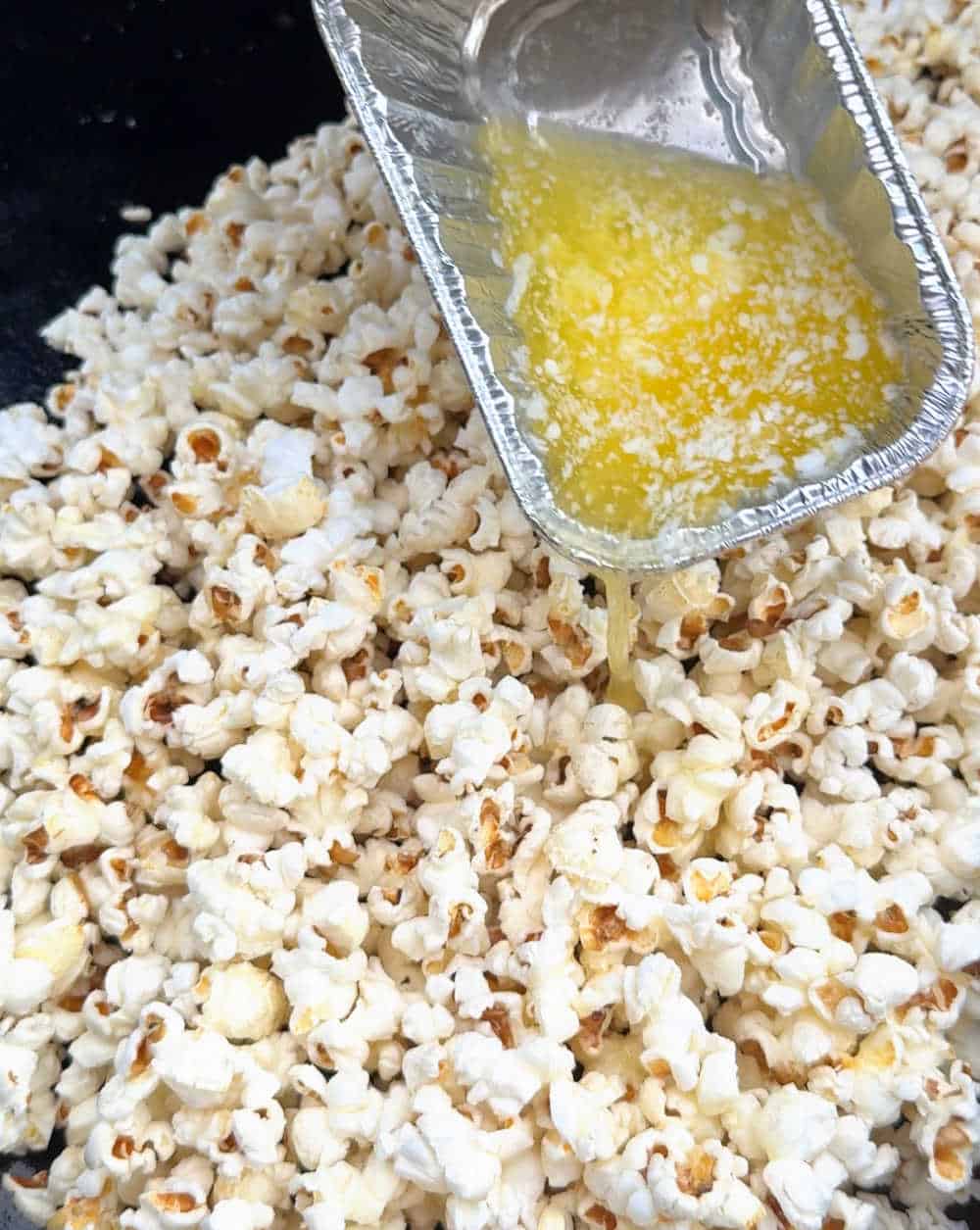 pouring melted butter over popped corn on Blackstone grill.