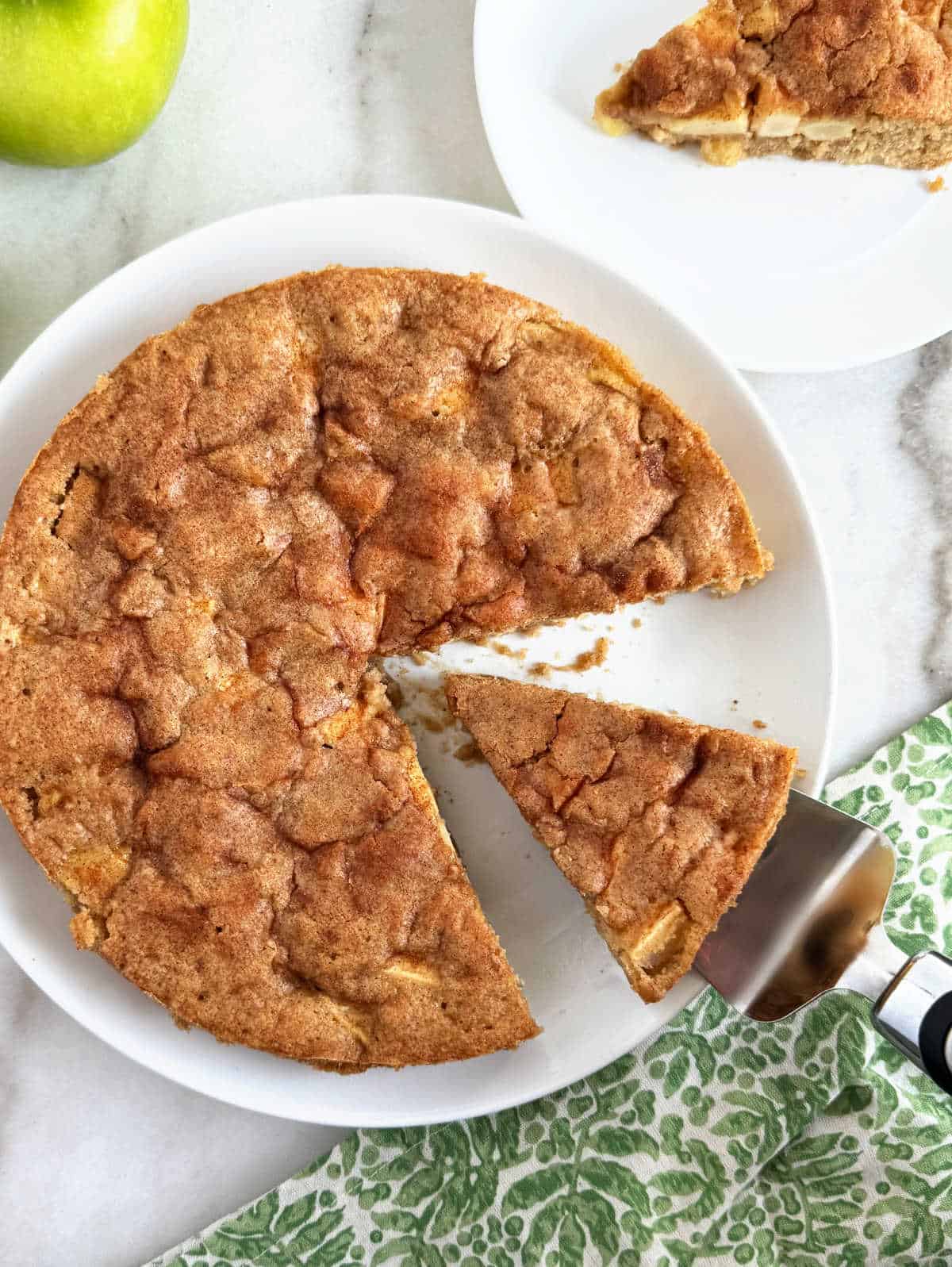 raw apple cake on platter with slice on cake server.