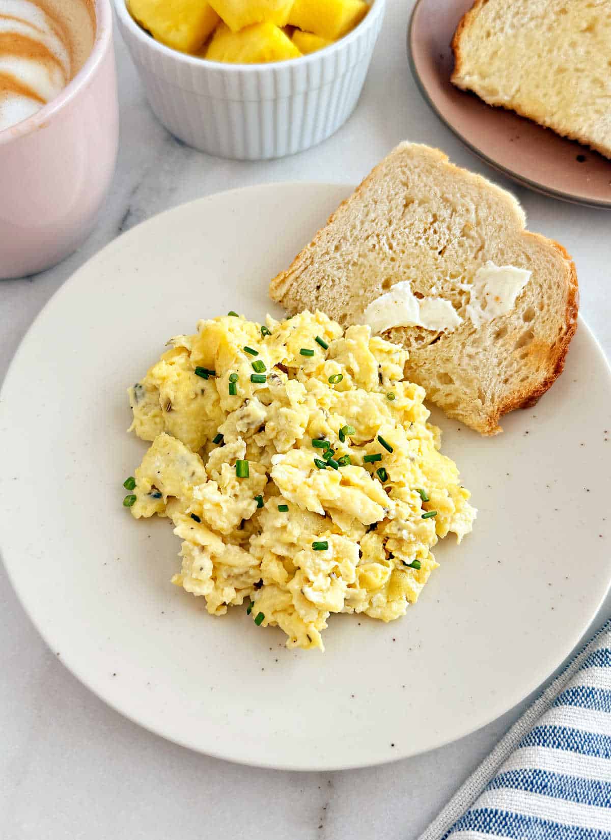 fluffy cream cheese scrambled eggs with chives and toast on plate.